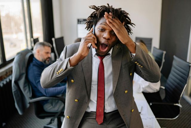A businessman with a surprised expression talks on his phone in an office setting.