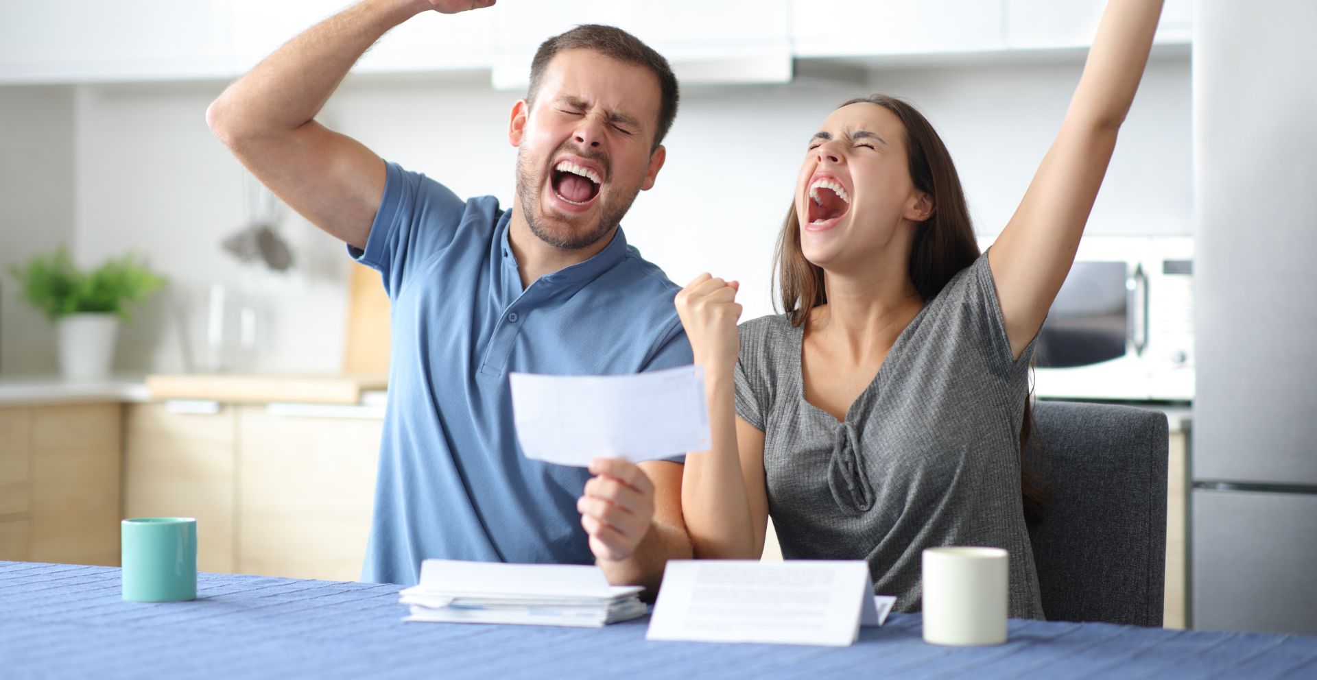 A shocked couple sitting at a table counting cash, illustrating financial surprise.